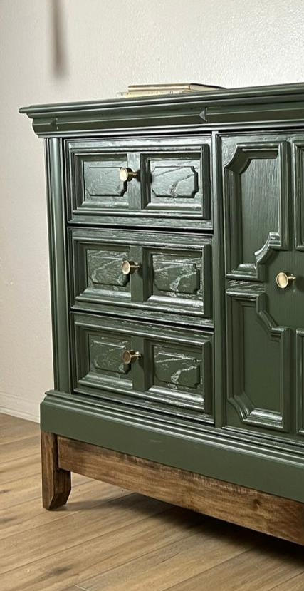 Close view of a green dresser’s raised drawer details, round metal knobs and wood base