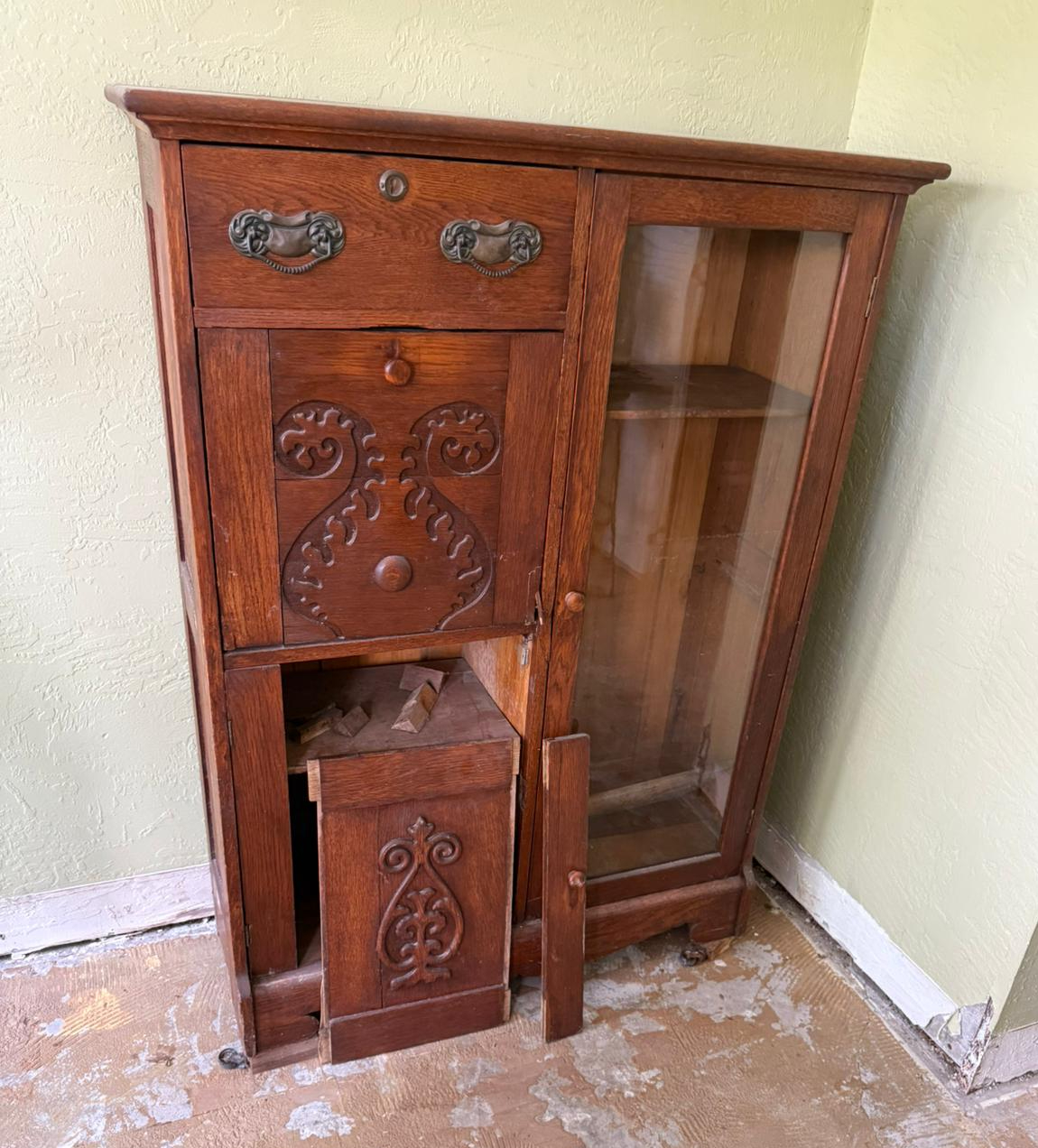 Ornate wood cabinet with a detached lower door resting in front of the opening