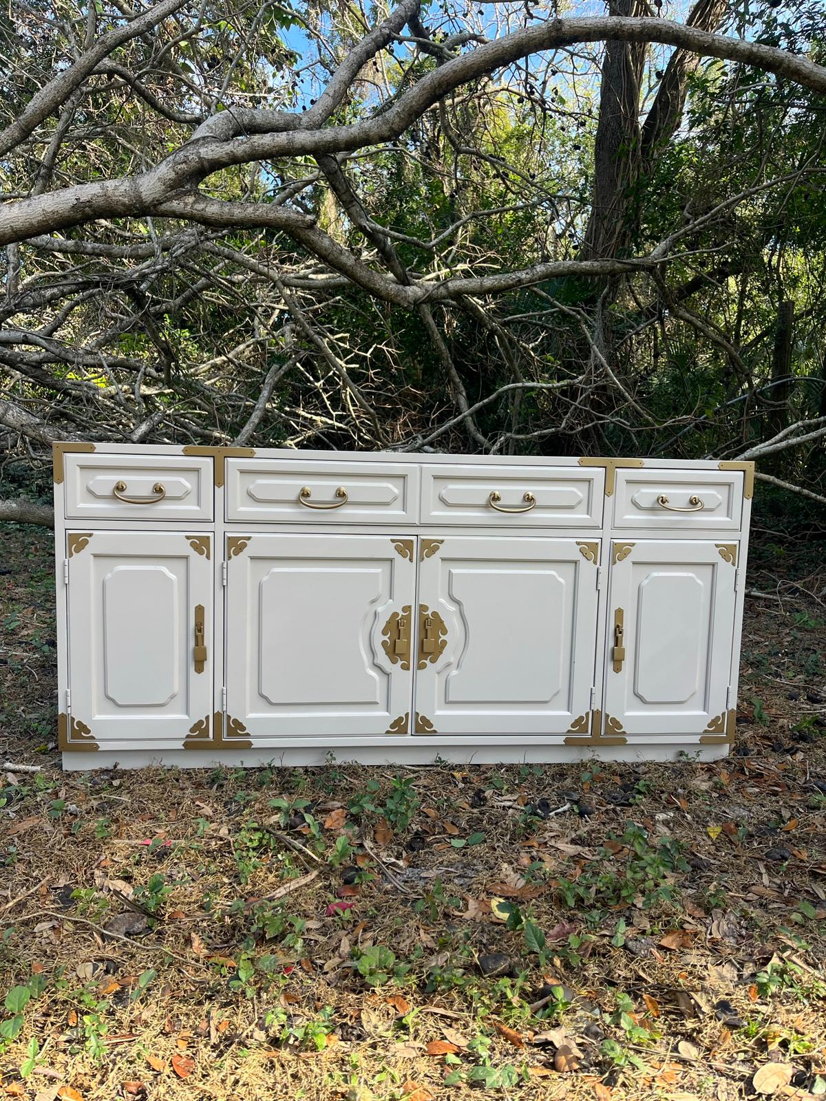 White sideboard with paneled doors, drawers, gold-tone handles and decorative metal fittings